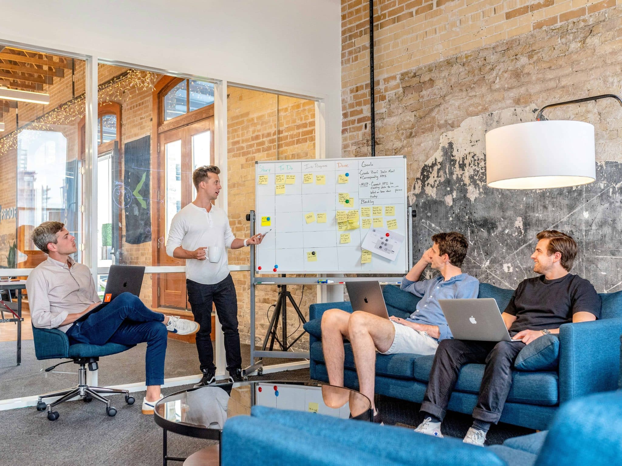 A small group of professionals collaborating during a team meeting with laptops and a whiteboard in a modern retreat space.