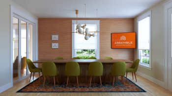 Board and dining room at Assemble Boise with long wooden table, green chairs, modern chandelier, and large screen for corporate meetings and retreats